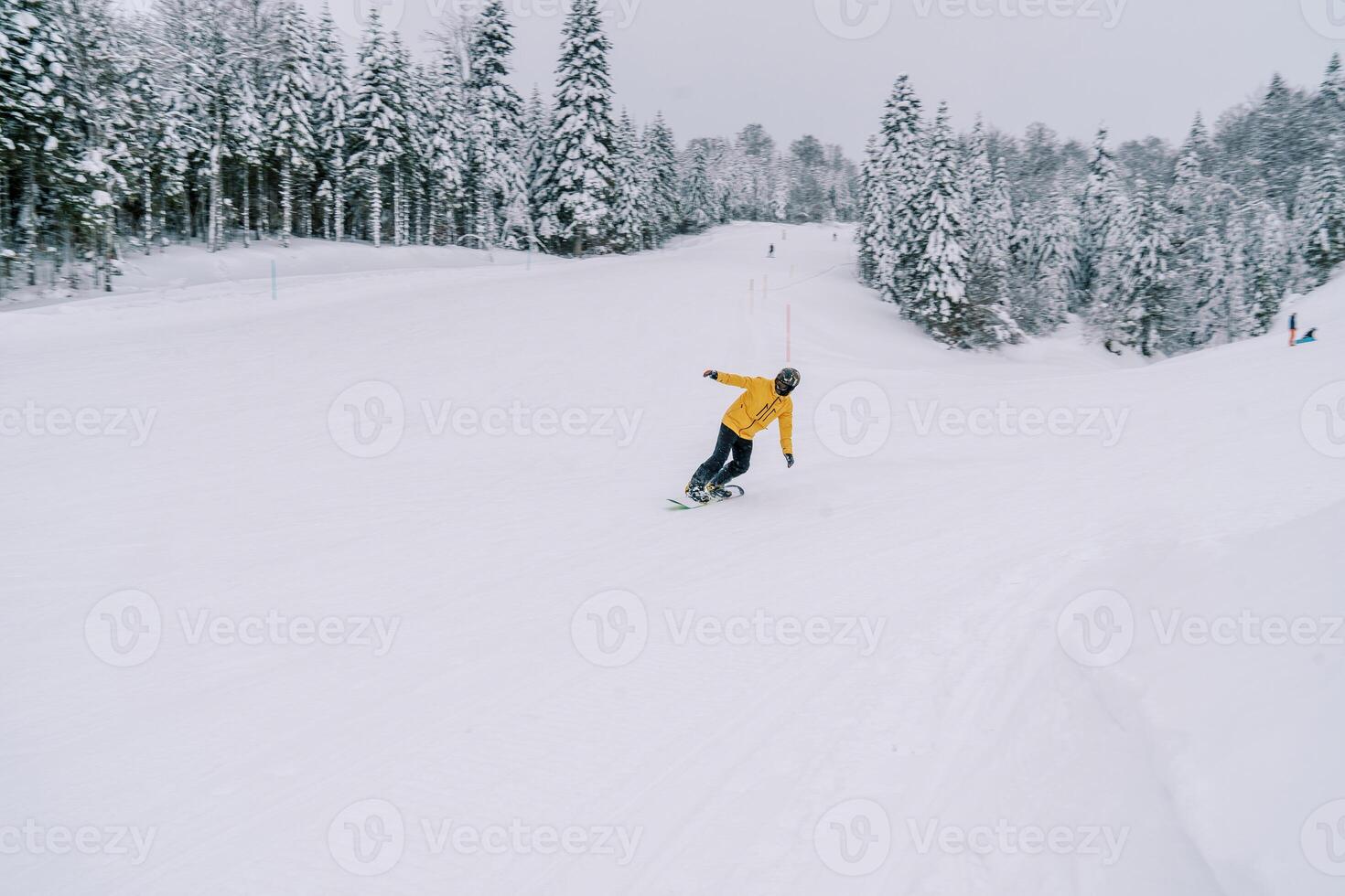 Snowboarder in a yellow ski suit rides a snowboard leaning to the side from a snowy mountain photo