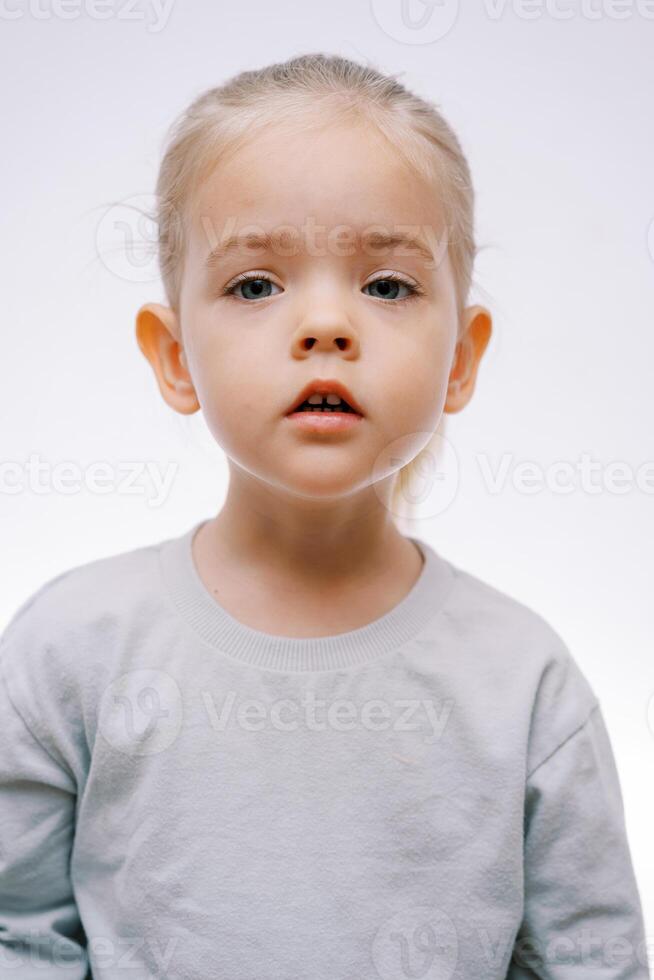 retrato de un pequeño esperando niña con su boca ligeramente abierto en un gris antecedentes foto