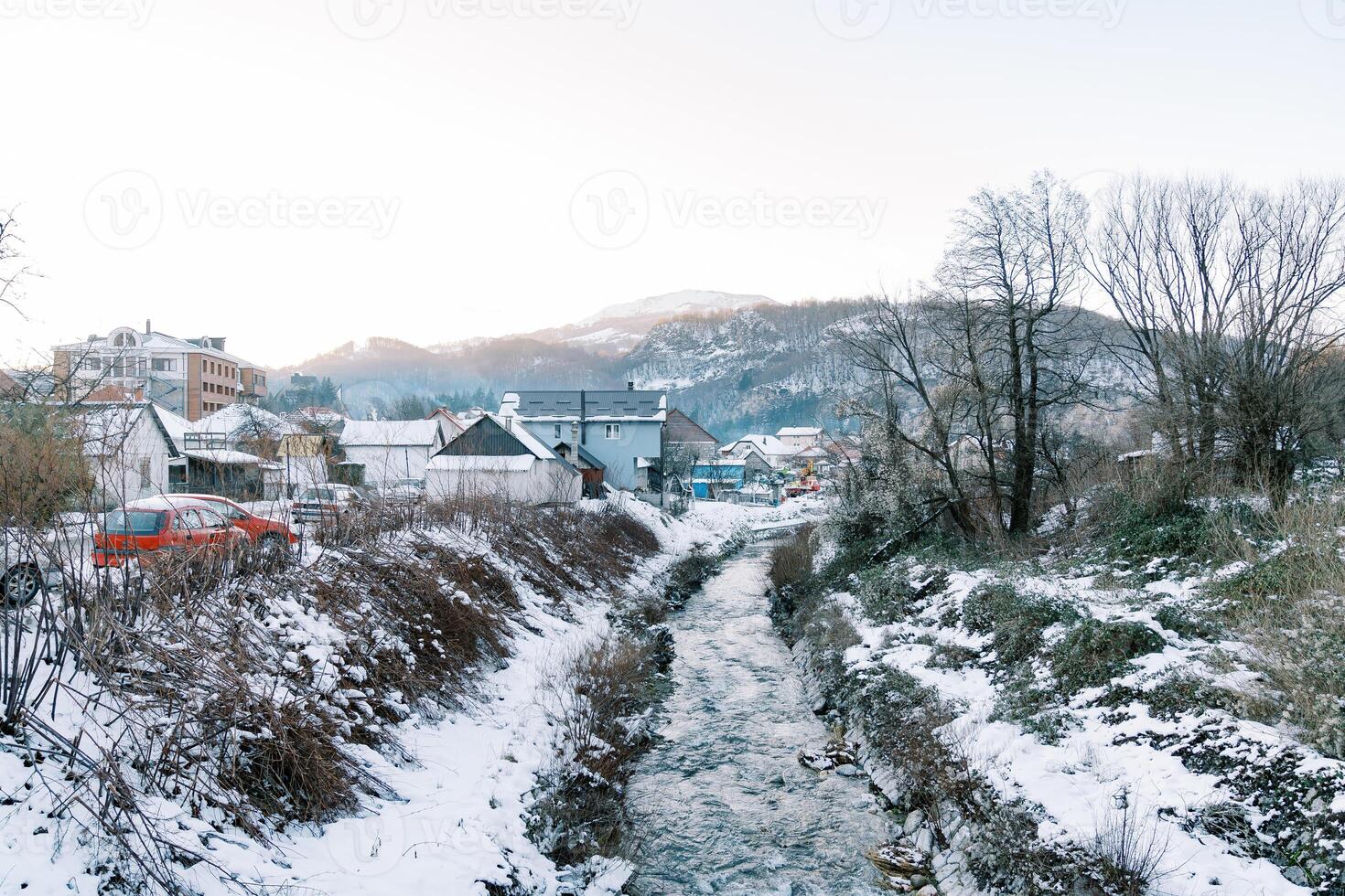 Mountain river flows between the snow-covered banks of a village at the foot of the mountains photo