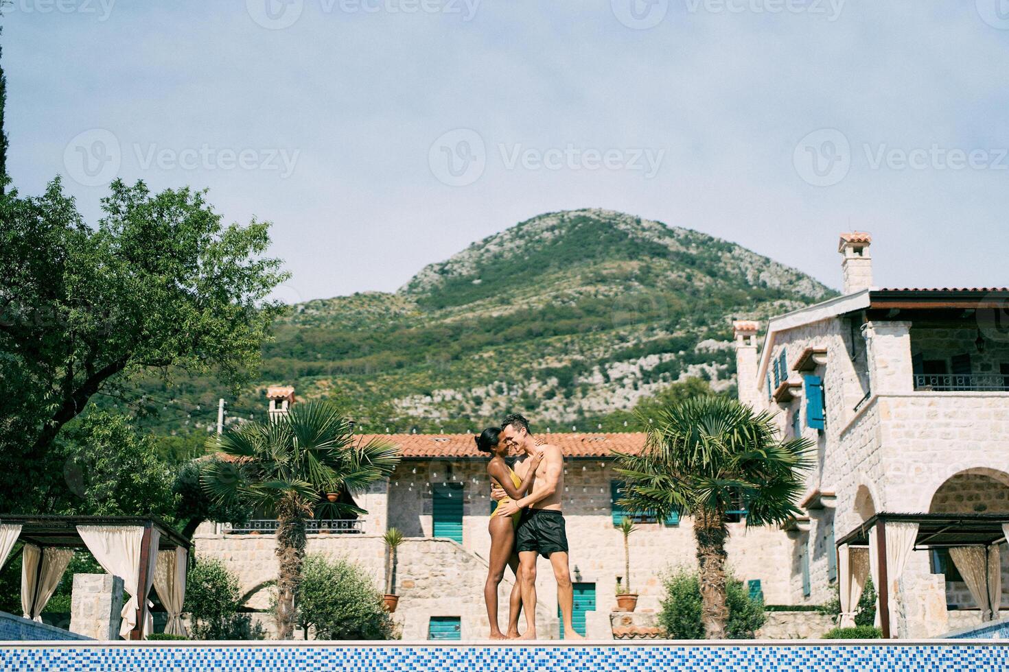 hombre y mujer abrazo mientras en pie por el piscina en frente de un antiguo villa foto