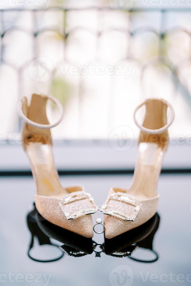 Engagement ring stands between the toes of the bride golden high-heeled shoes on the mirror floor photo