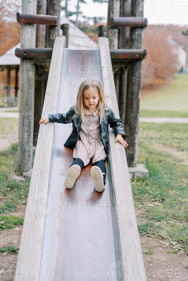 Little girl slides down a slide on a playground holding the handrails photo