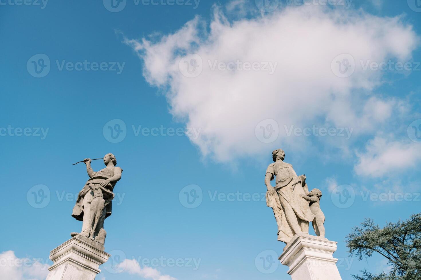 Ancient statues on stone pedestals of the fence of an old villa against a blue sky photo