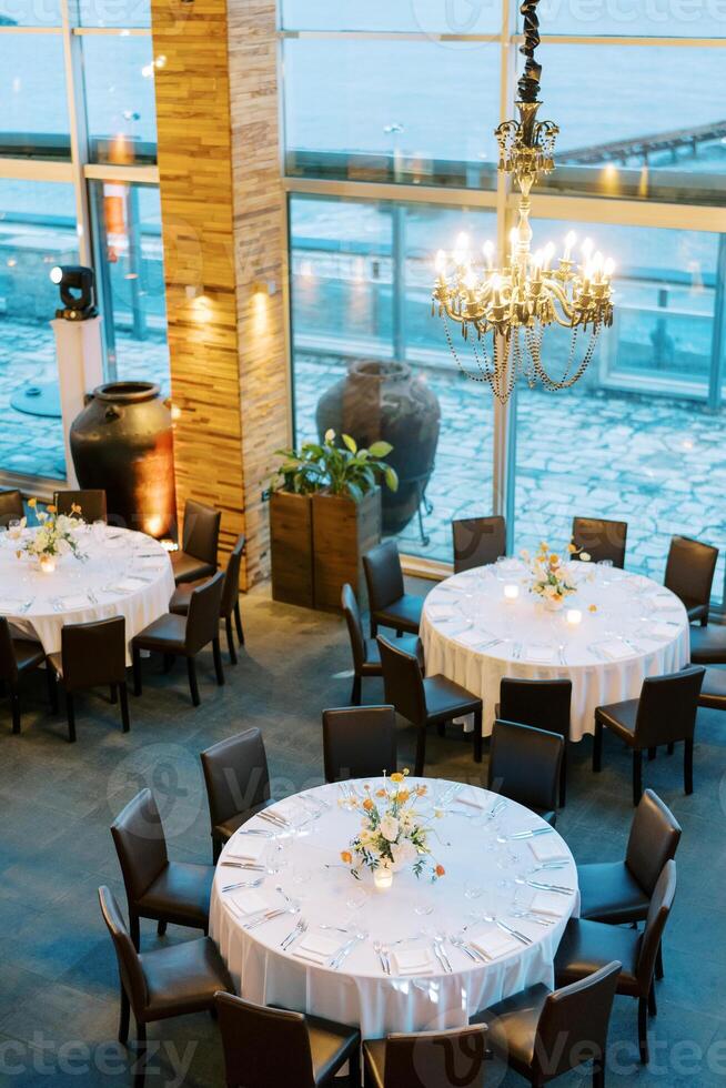 Set round festive tables in a restaurant with large windows and high ceiling photo
