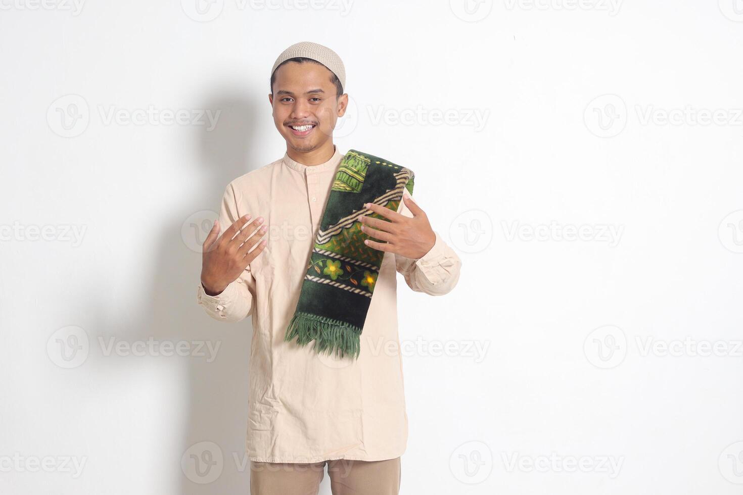 Portrait of attractive Asian muslim man in koko shirt with skullcap inviting and welcoming someone to come in. Isolated image on white background photo