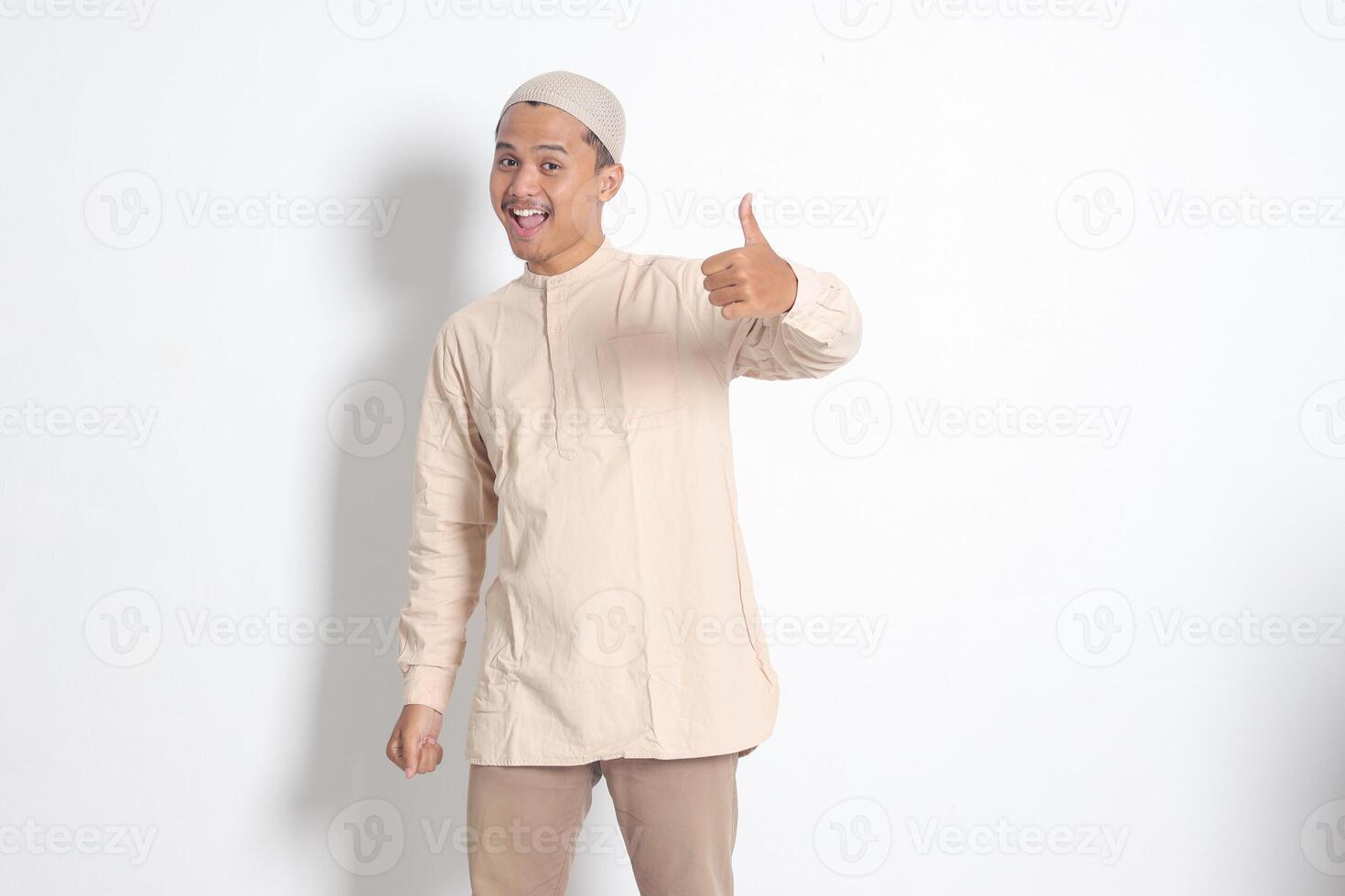 Portrait of attractive Asian muslim man in koko shirt showing thumb up, good job hand gesture. Approval concept. Isolated image on white background photo