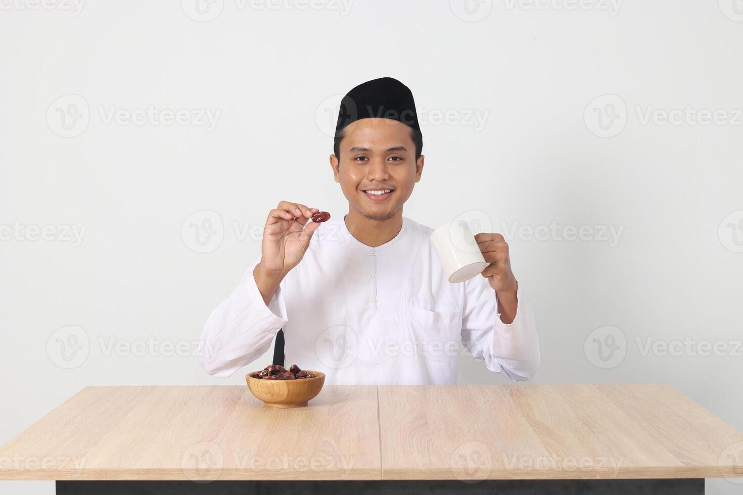 Portrait of excited Asian muslim man eating kurma or date fruit during sahur and breaking fast. Culture and tradition on Ramadan month. Isolated image on white background photo