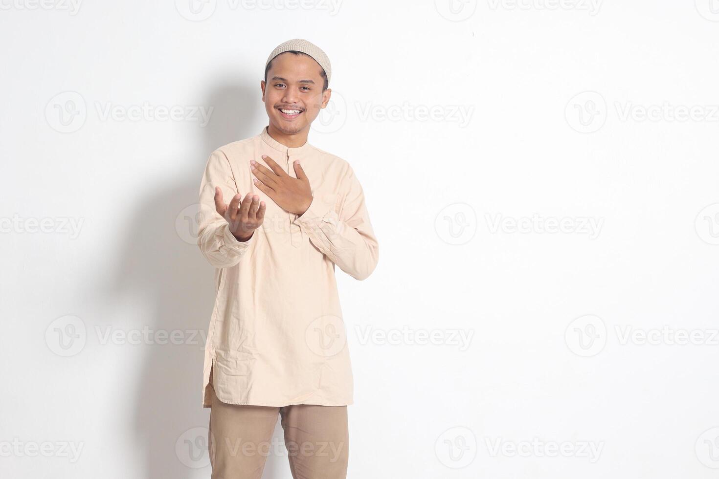 Portrait of attractive Asian muslim man in koko shirt with skullcap inviting and welcoming someone to come in. Isolated image on white background photo