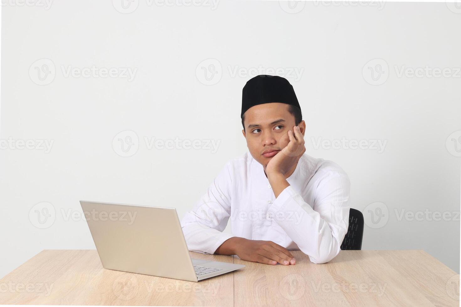 Portrait of tired Asian muslim man in koko shirt with skullcap working during fasting on ramadan month, feeling sleepy, yawning with hand covering mouth. Isolated image on white background photo