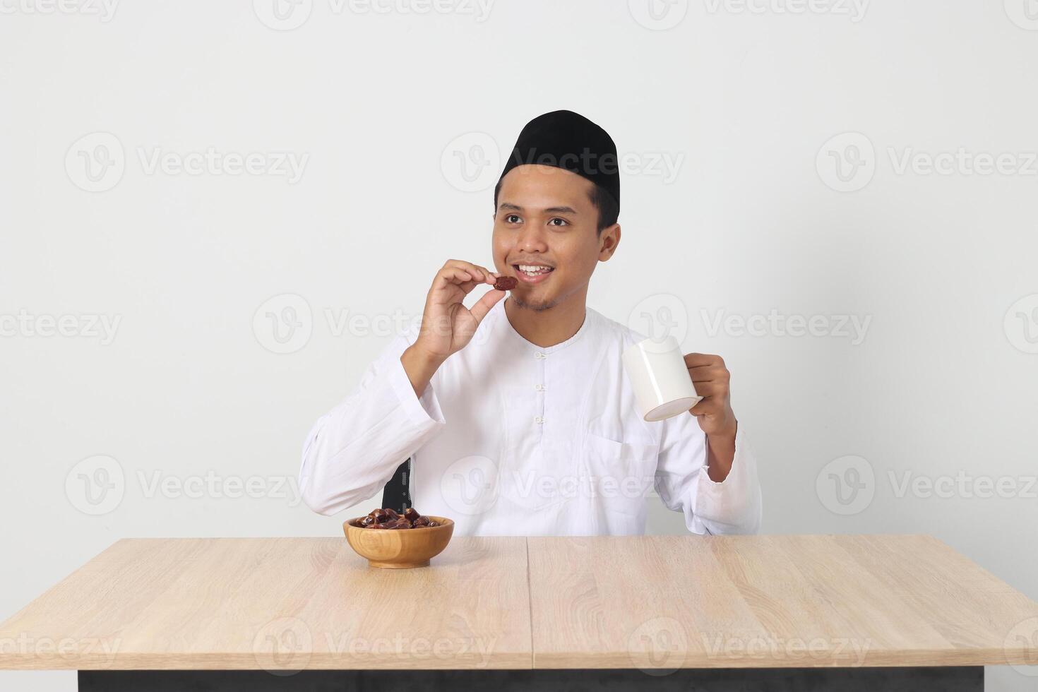 Portrait of excited Asian muslim man eating kurma or date fruit during sahur and breaking fast. Culture and tradition on Ramadan month. Isolated image on white background photo