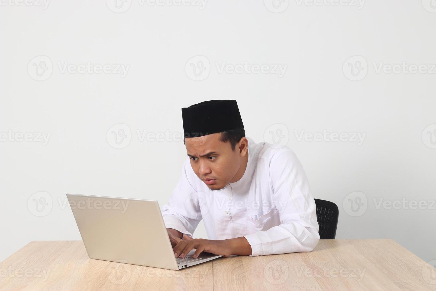 retrato de emocionado asiático musulmán hombre en koko camisa con casquete trabajando en su ordenador portátil durante rápido en Ramadán mes. aislado imagen en blanco antecedentes foto