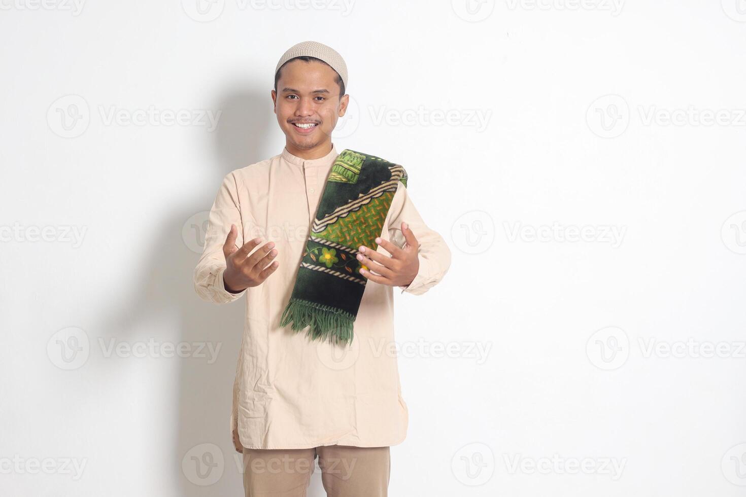 Portrait of attractive Asian muslim man in koko shirt with skullcap inviting and welcoming someone to come in. Isolated image on white background photo