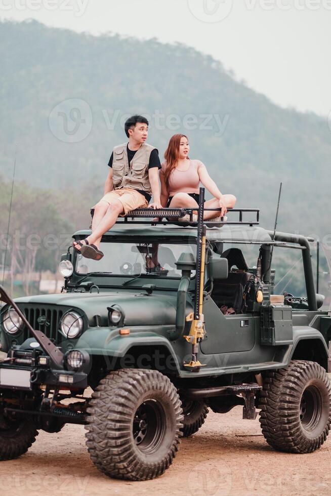 Perched atop their off road car, a couple sits closely together, taking in the beauty of rolling hills stretching into the distance. photo