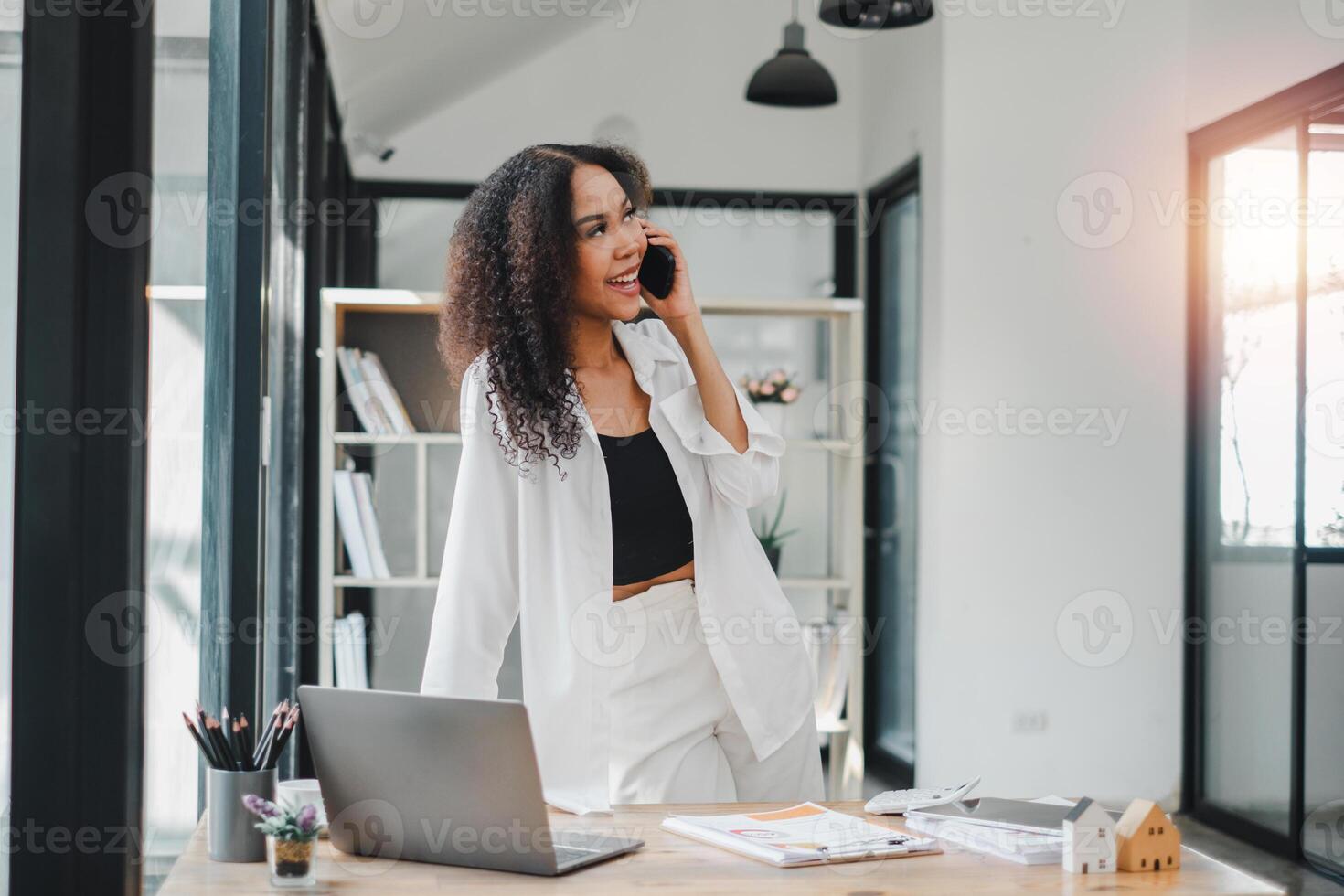 Happy freelancer using computer and talking on smart phone at home office photo