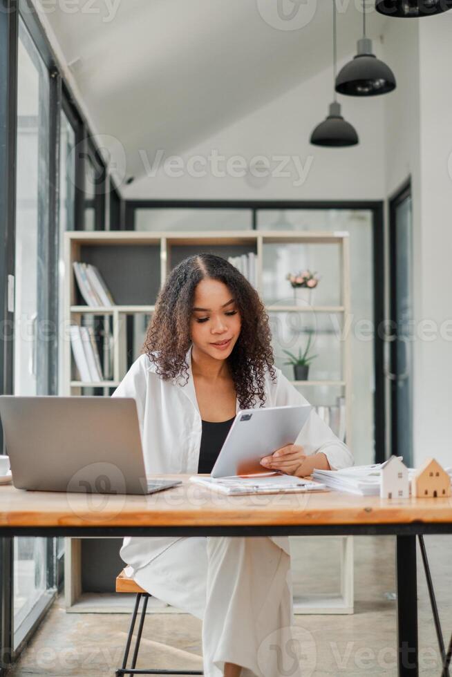 Real estate agent attentively reviews property documents with a laptop open on her desk in a contemporary, chic office setting. photo