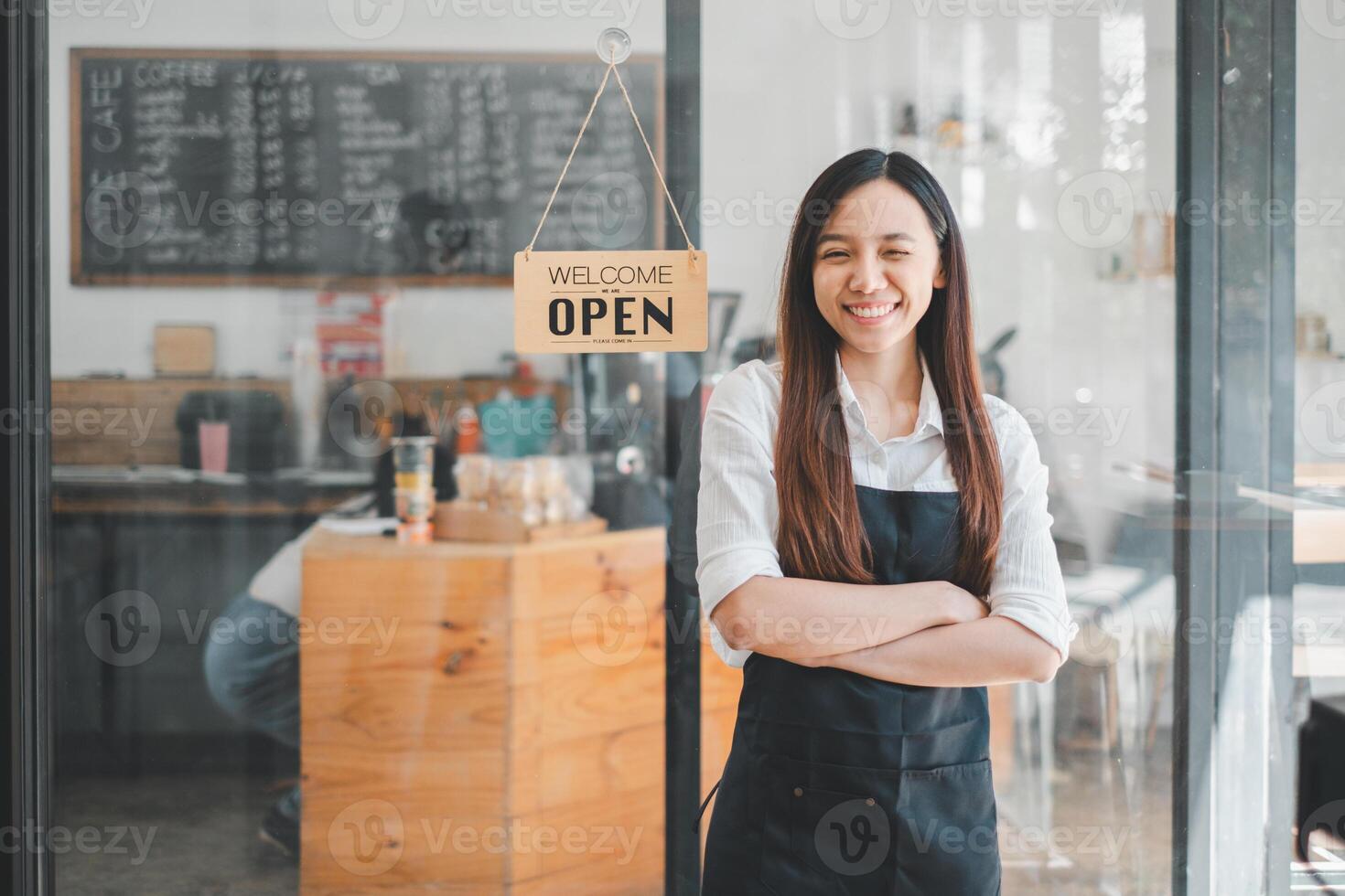 Welcoming cafe owner with arms crossed, smiling in front of her business with an open sign, portraying entrepreneurship and customer service. photo