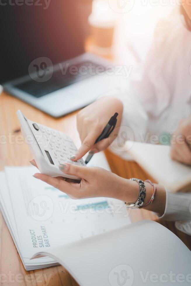 Close up of a business professional using a calculator for financial analysis over important documents with a laptop in the background. photo