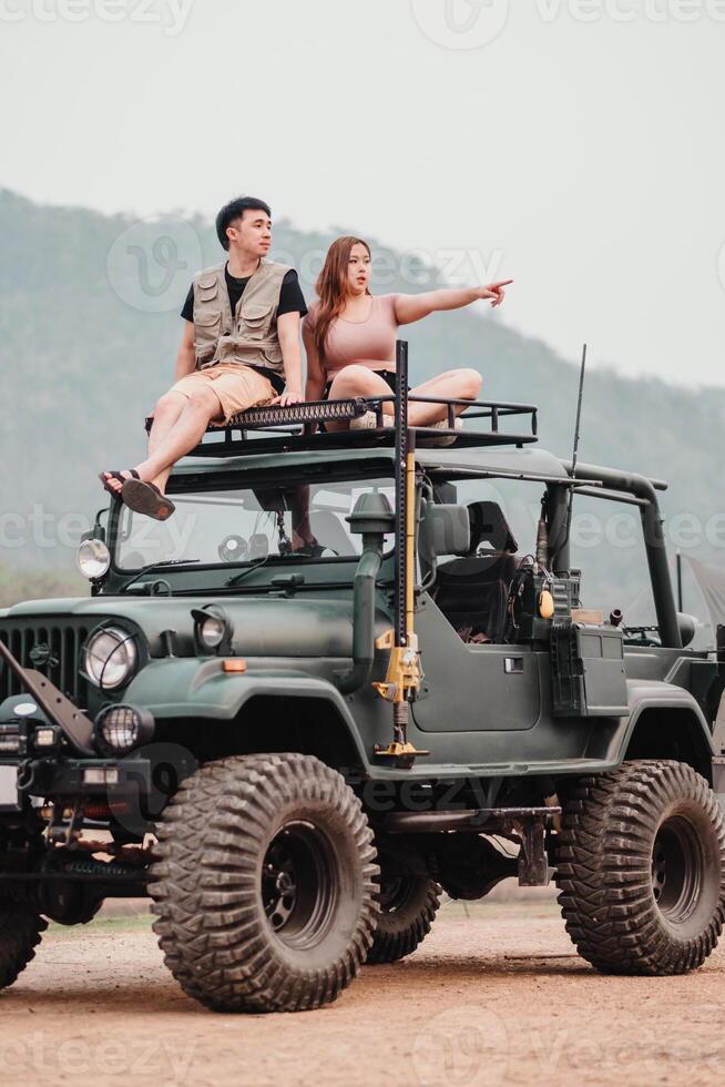 Adventurous couple is perched atop a rugged car, the woman pointing towards the horizon, ready for their next off-road exploration. photo