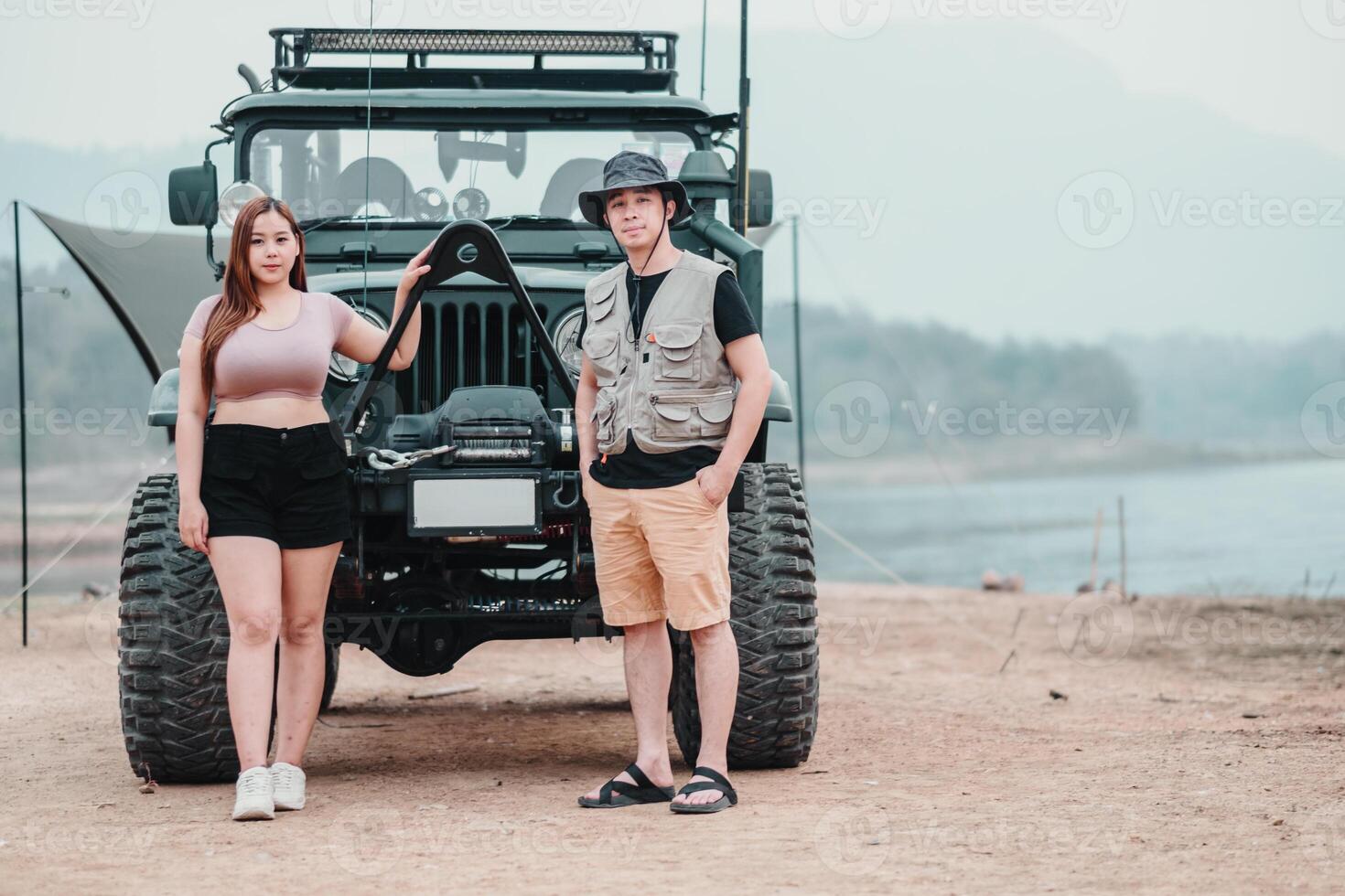 Confident couple stands proudly by their car at a campsite, showcasing their adventurous spirit and readiness for outdoor exploration. photo