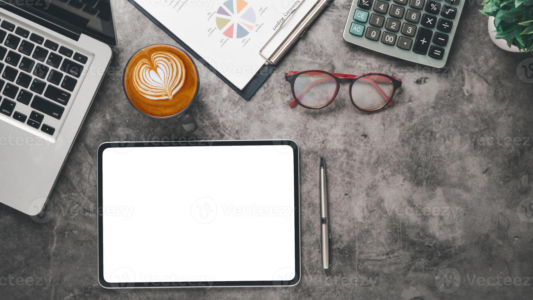 An aerial view of a modern work desk with a tablet, laptop, coffee with latte art, calculator, and report for a productive day. photo