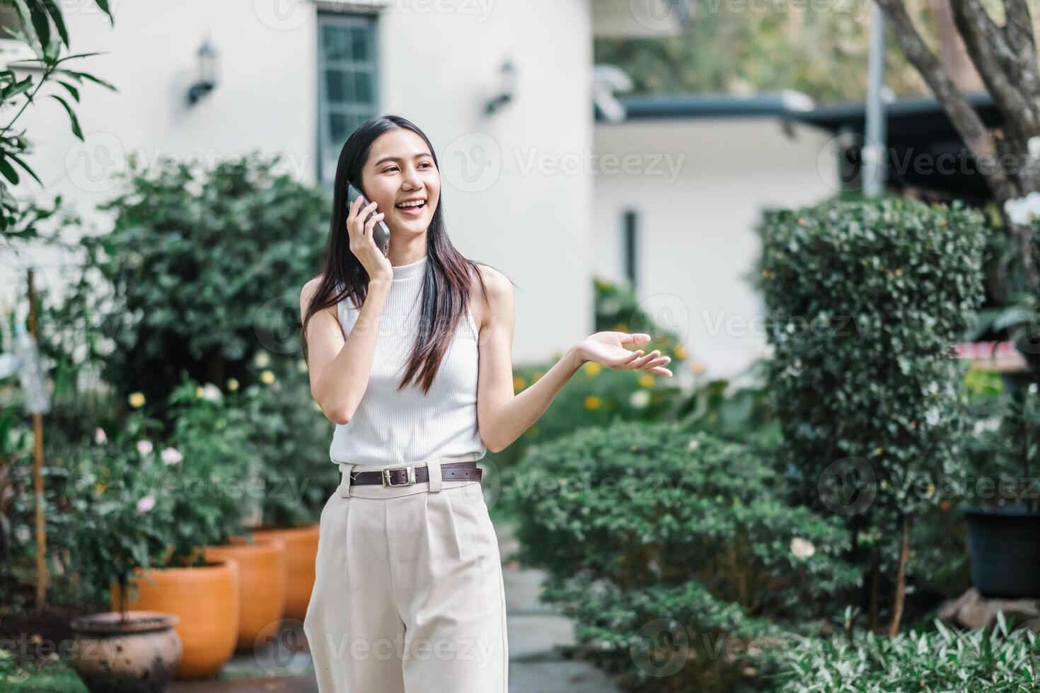 alegre mujer de negocios tiene un agradable conversacion en su teléfono mientras caminando en un lozano jardín ajuste. foto