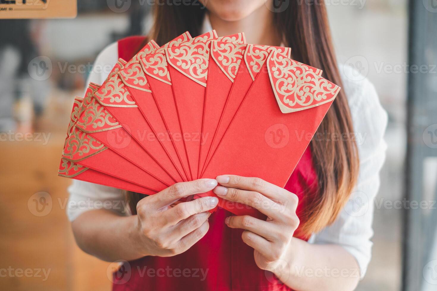 A close-up of a woman holding a fan of ornate red envelopes, a traditional symbol of luck and prosperity in Asian cultures, often exchanged during special occasions. photo