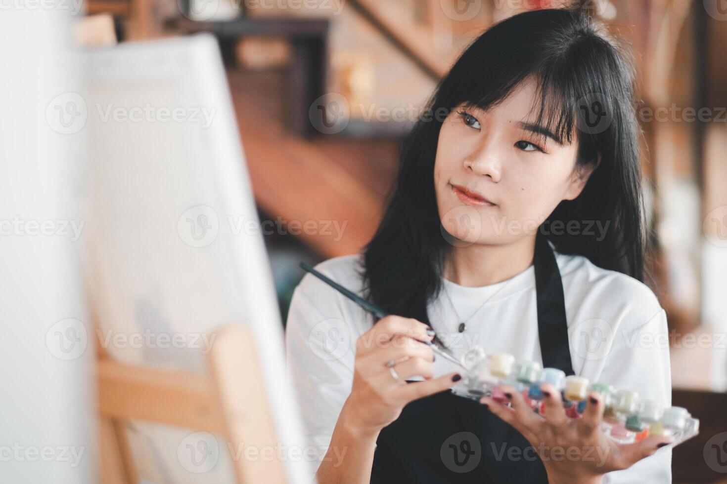 An aspiring artist with a serene expression delicately applies brush strokes to a canvas in a cozy, well-decorated studio filled with creative inspiration. photo