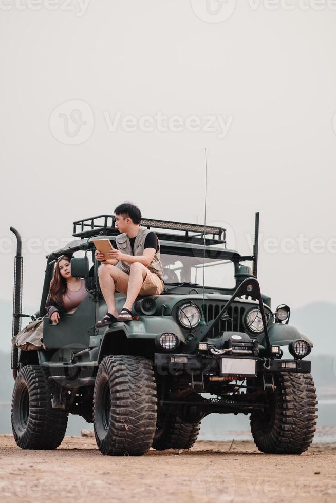 Young couple is deep in discussion over a notebook, comfortably seated atop their modified car, set against a hazy mountain landscape. photo