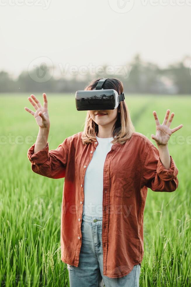 In a verdant rice field at dusk, a woman with a VR headset reaches out, exploring a digital world beyond the natural landscape. photo