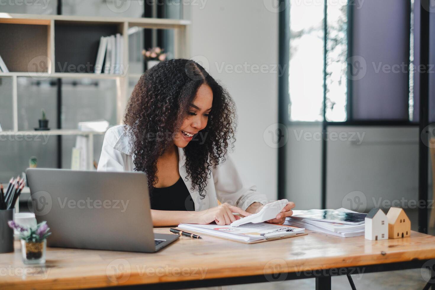 Attractive hardworking businesswoman with Afro hairstyle busy doing paperwork at office desk, working through finances, using calculator photo