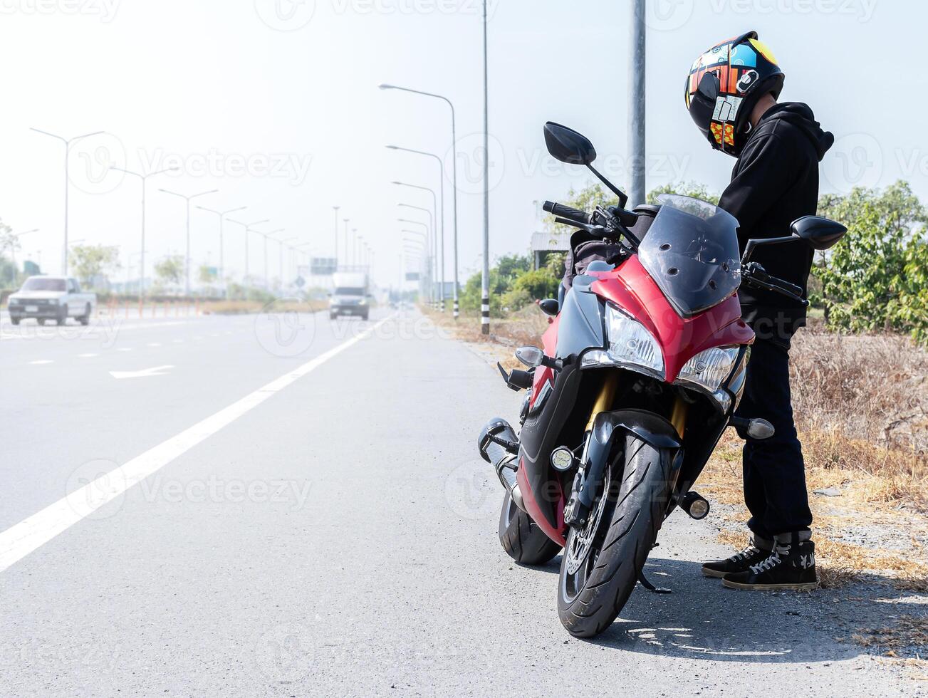 Biker man standing with motorcycle parked on side of road photo