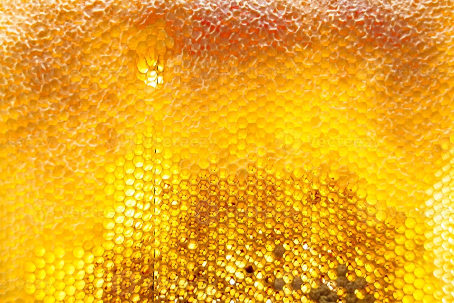 Drop of bee honey drip from hexagonal honeycombs filled with golden nectar photo