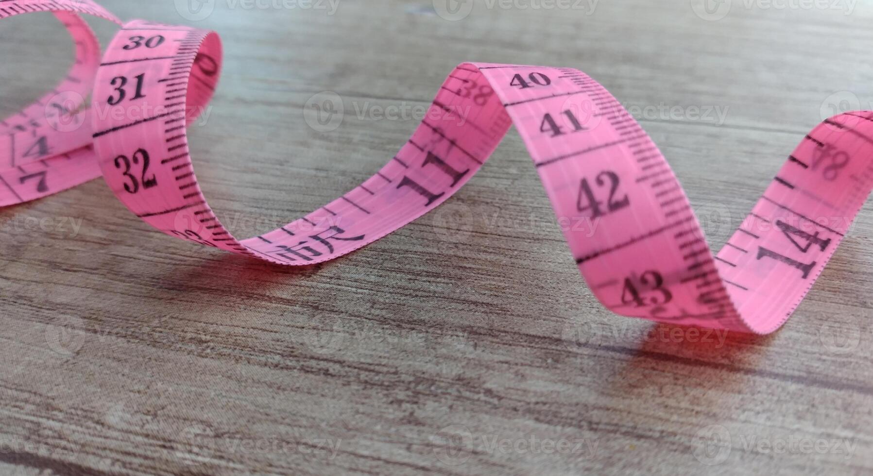 pink measuring tape on a wood background. Rolled tape with numbers photo