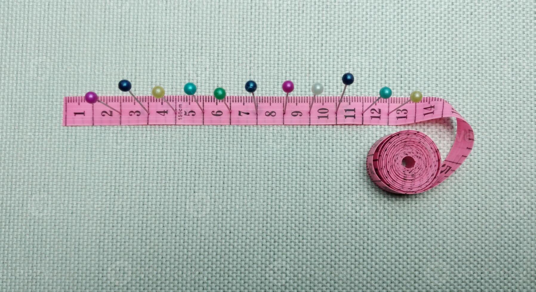 sewing needles and pins of different colors, ruler on white cloth background photo