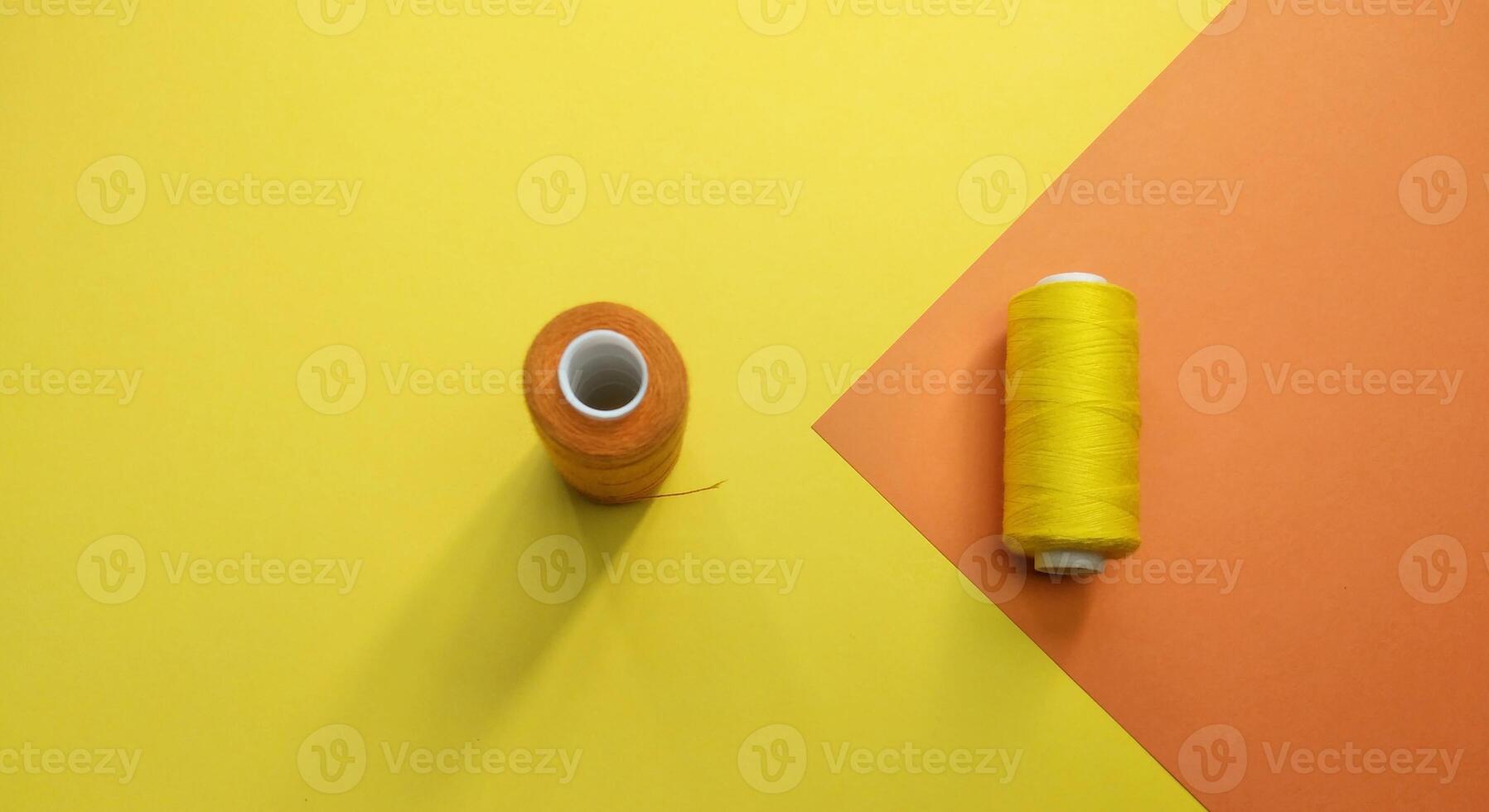 Spools of thread and a needle on a yellow and orange background, Contrast consept photo