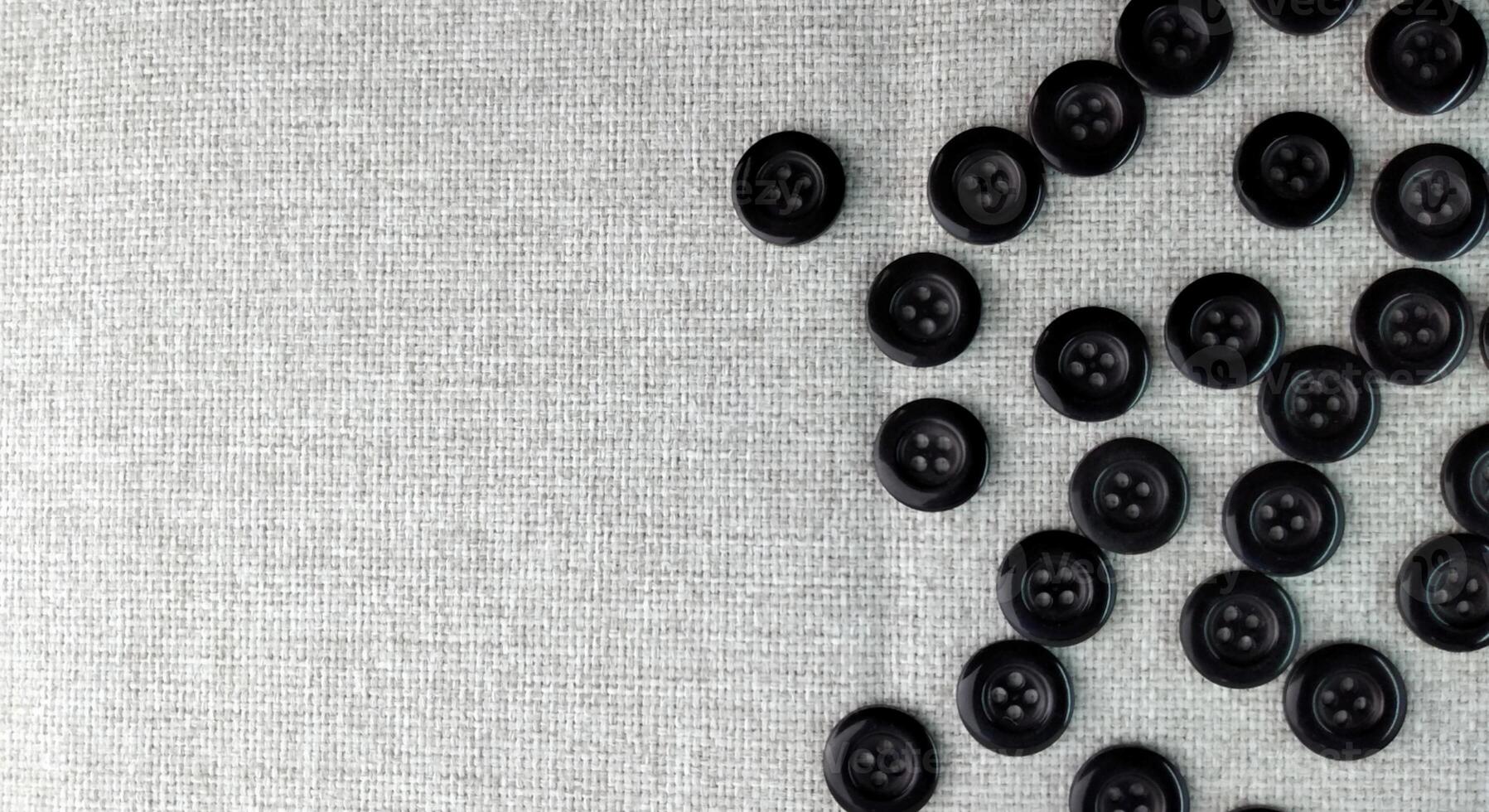Black sewing buttons on white fabric background. Flat lay, top view. photo