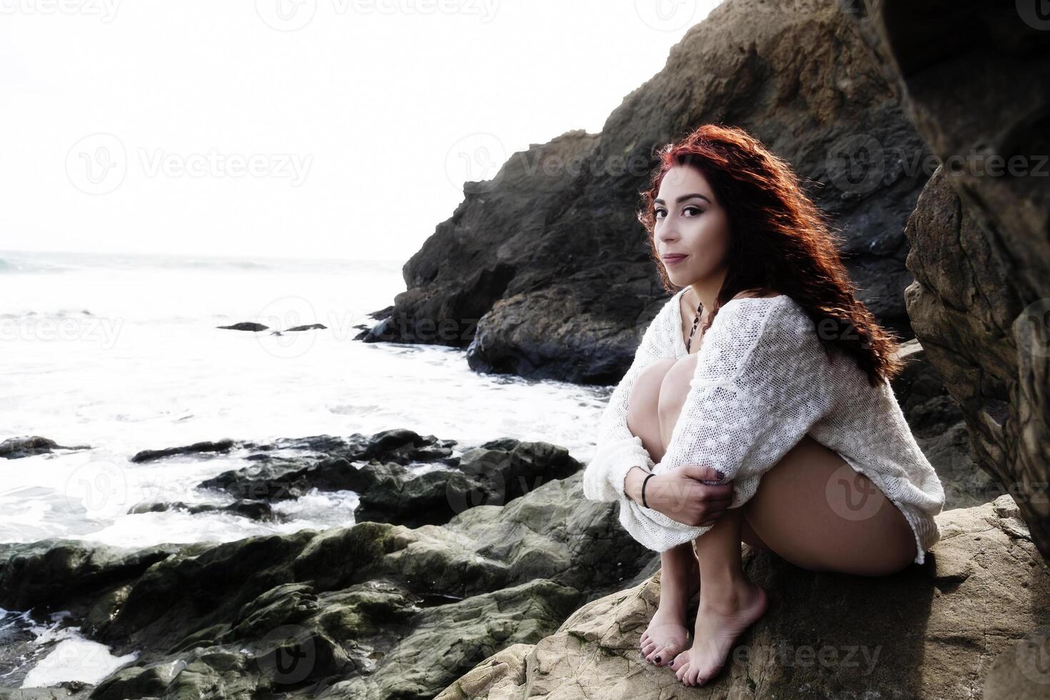 Latina Woman Sitting On Rocks At Ocean photo