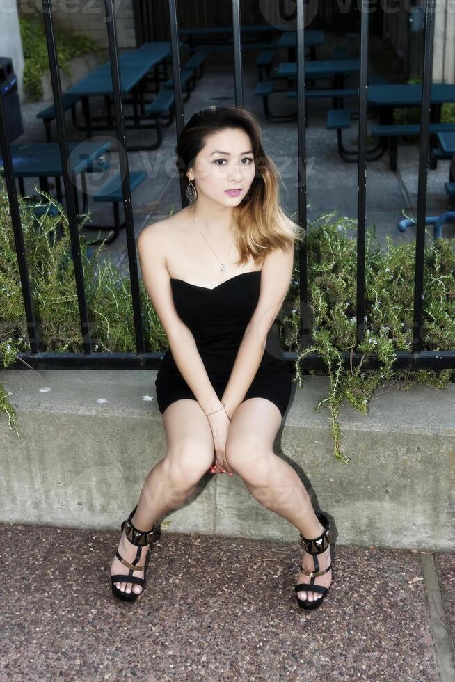 Asian American Woman Sitting On Cement Curb photo