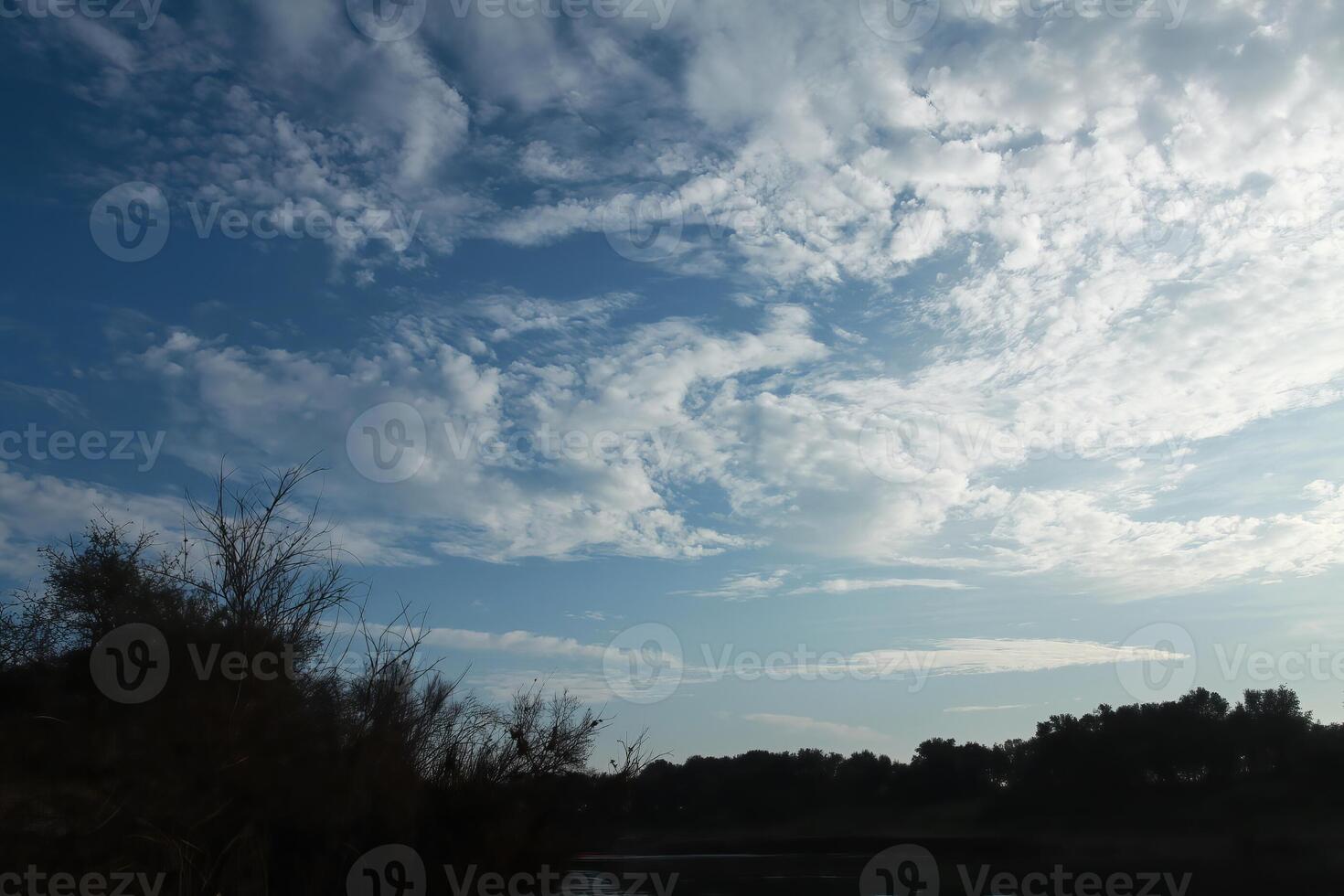 White Clouds In Blue Sky Over Silhouetted Landscape photo