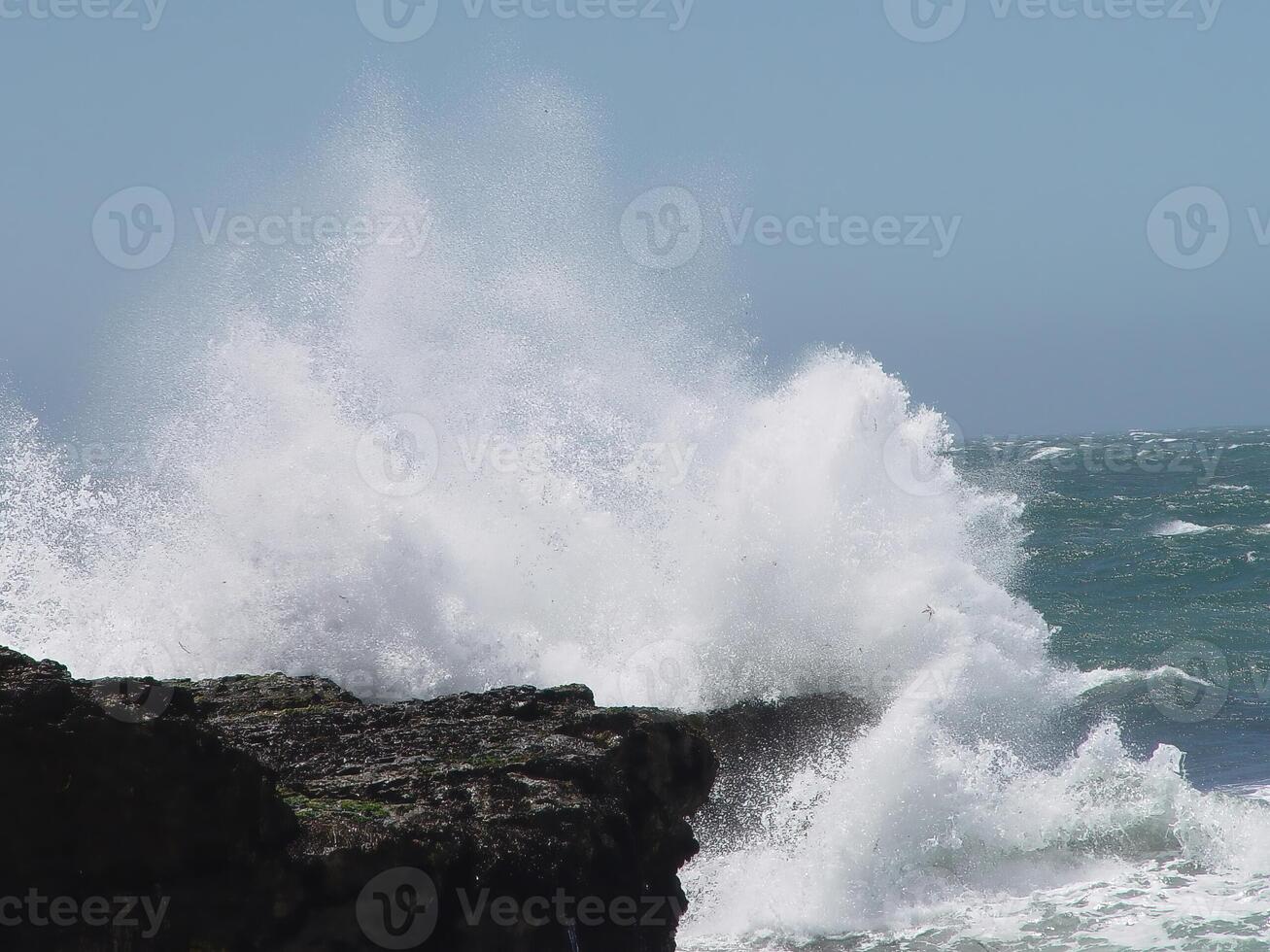 Ocean Wave Crashing Into Rock Shore With Blue Sky photo