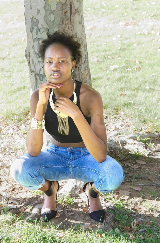 joven africano americano adolescente al aire libre en cuclillas en pantalones foto