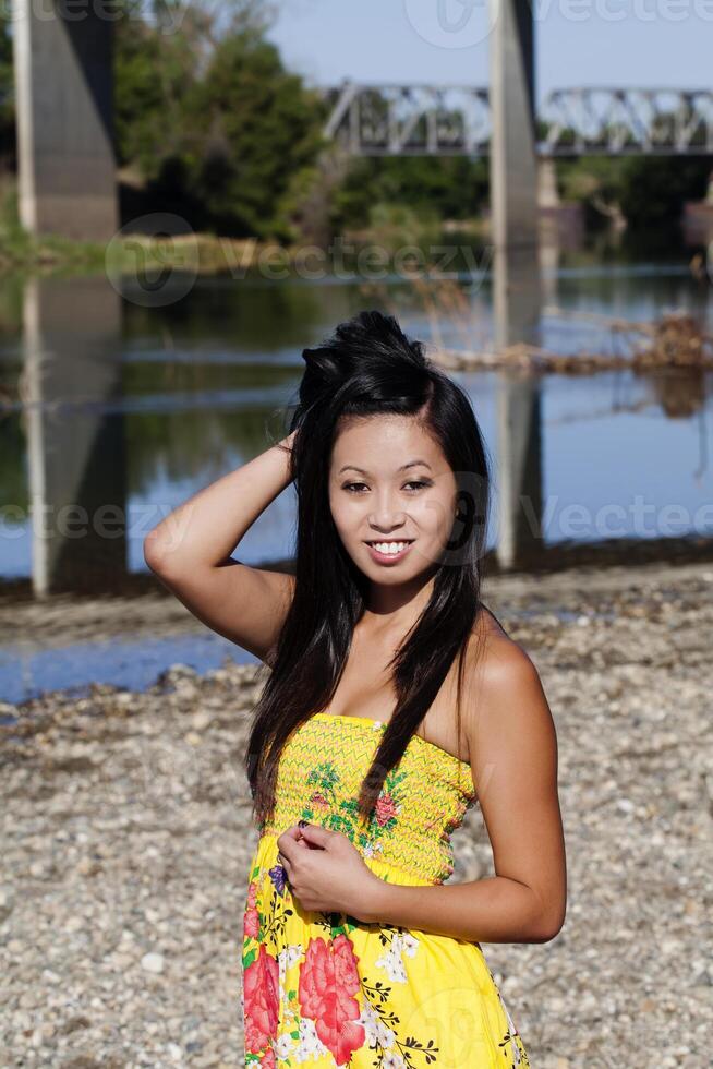 asiático americano mujer amarillo vestir río sonriente foto