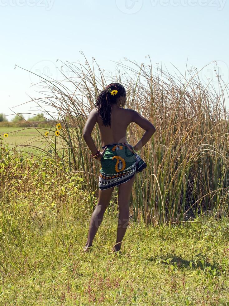 Young black woman in field bare top from back photo