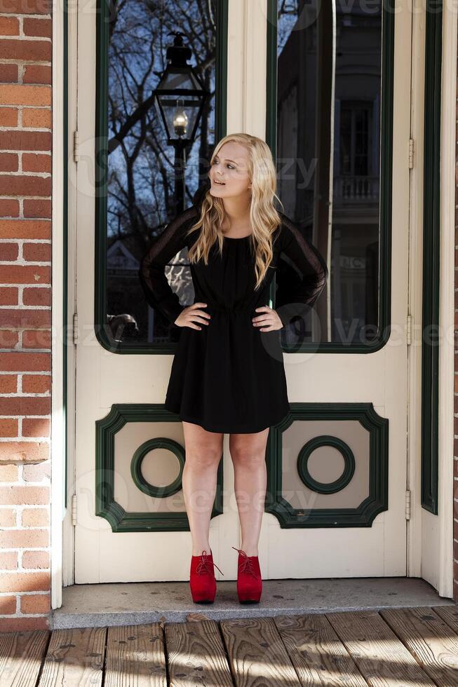 Attractive Young Blond Woman Standing Black Dress Red Shoes photo