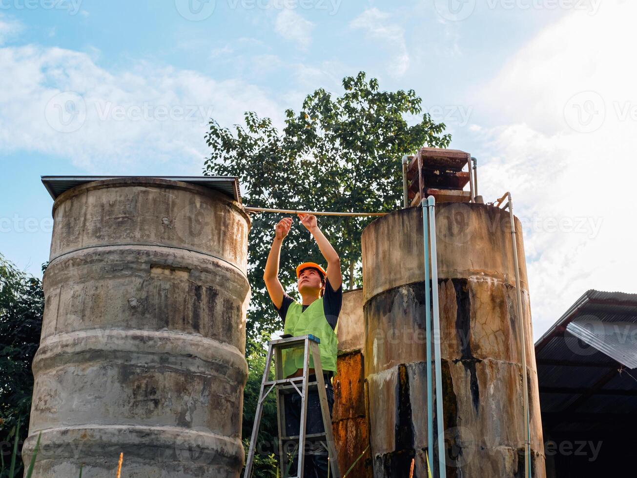 ingeniero que controla la calidad del agua se encuentra en las escaleras de riesgo en lugares altos operando equipos de filtración o purificación de agua industrial viejos tanques de cemento para mantener el agua en la fábrica de agua foto