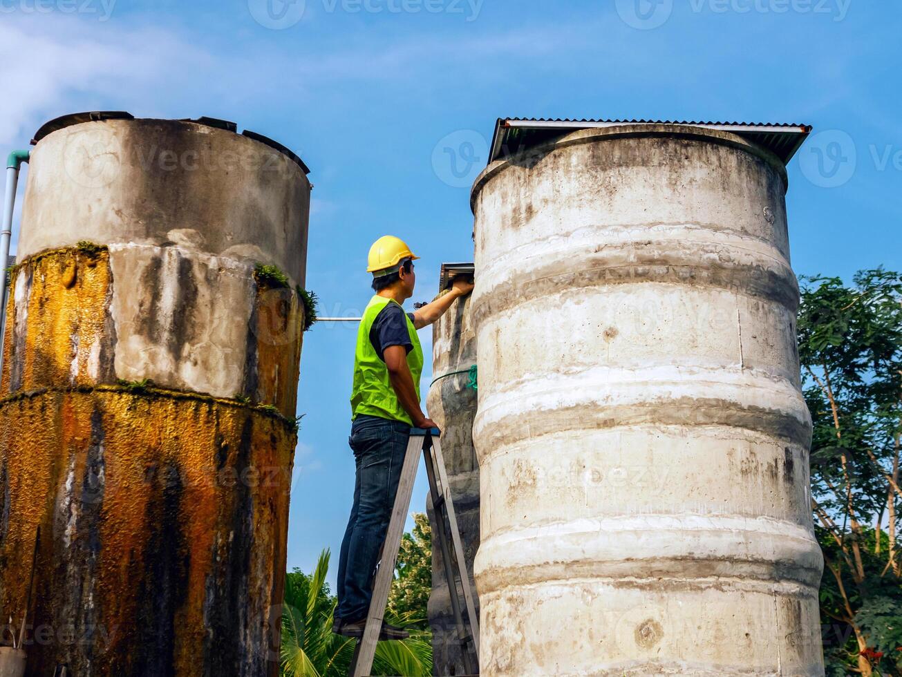 ingeniero que controla la calidad del agua se encuentra en las escaleras de riesgo en lugares altos operando equipos de filtración o purificación de agua industrial viejos tanques de cemento para mantener el agua en la fábrica de agua foto