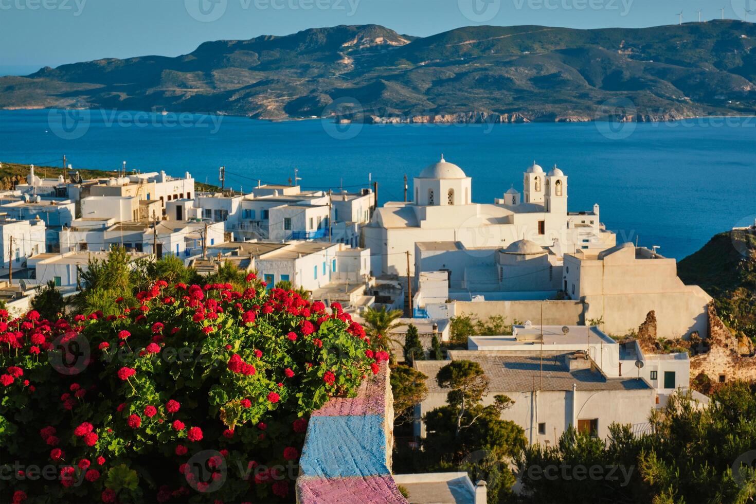Picturesque scenic view of Greek town Plaka on Milos island over red geranium flowers photo