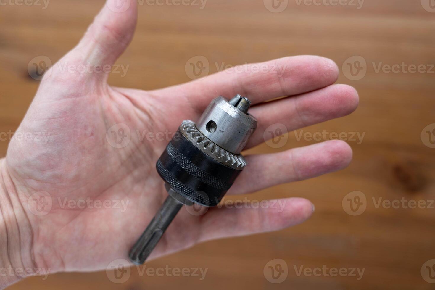 A man's hand holds a drill chuck. wooden background photo