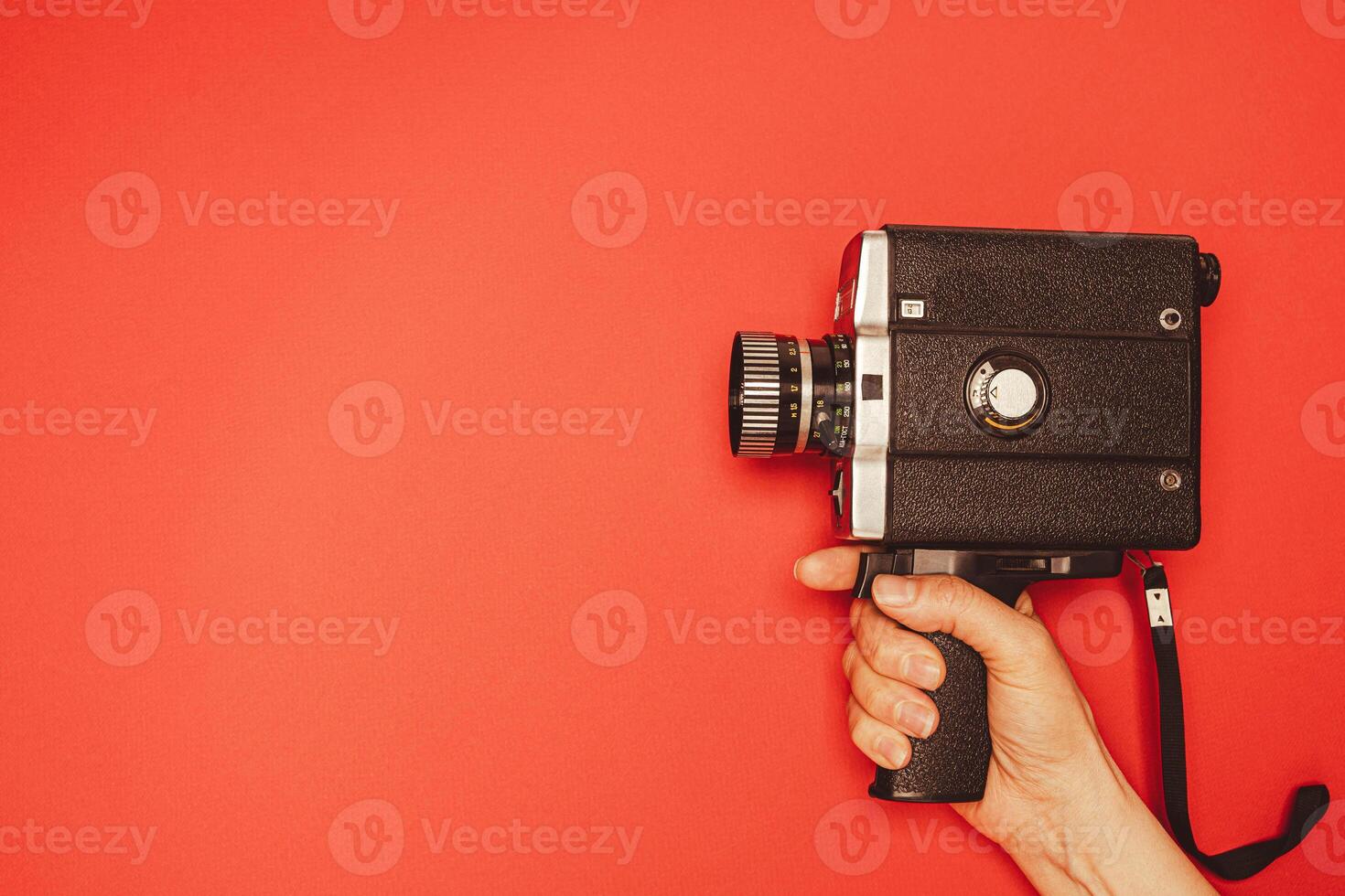 vintage portable movie camera in a woman's hand on a red background. retro, 70s, 80s photo