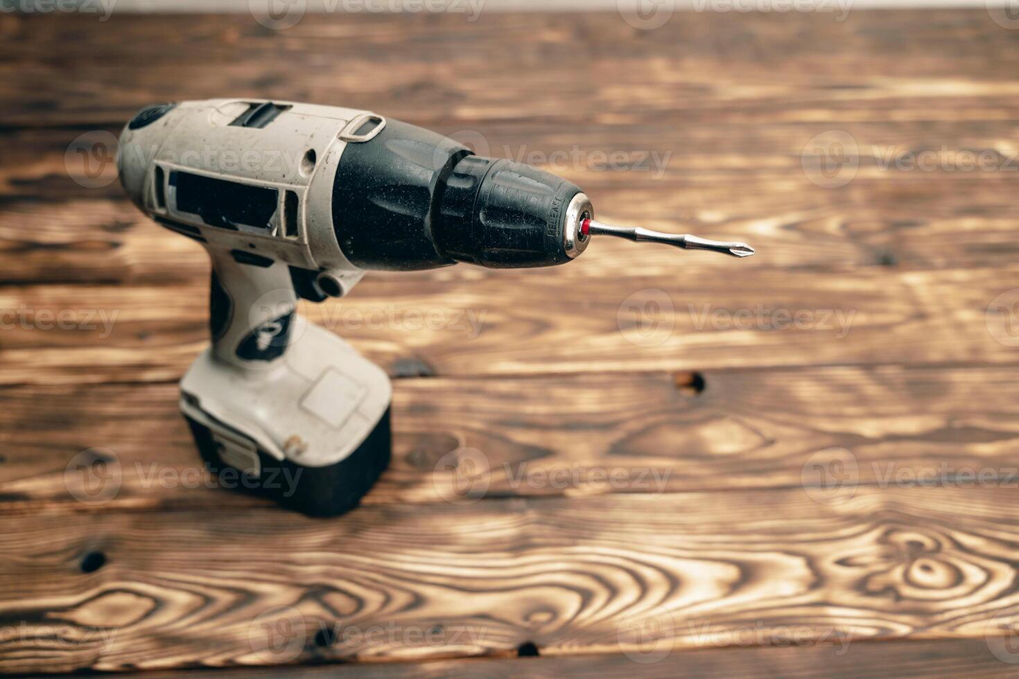 There is a cordless drill on a wooden table. A working tool. DIY concept photo